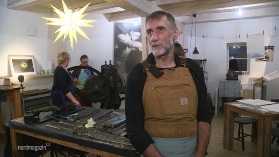 Ein Mann in Arbeitskleidung in einer Werkstatt. © Screenshot 