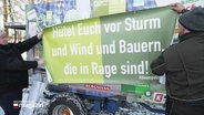 Eine Frau und ein Mann halten ein Plakat mit der Aufschrift "Hütet euch vor Sturm und Wind und Bauern, die in Rage sind!" © Screenshot 