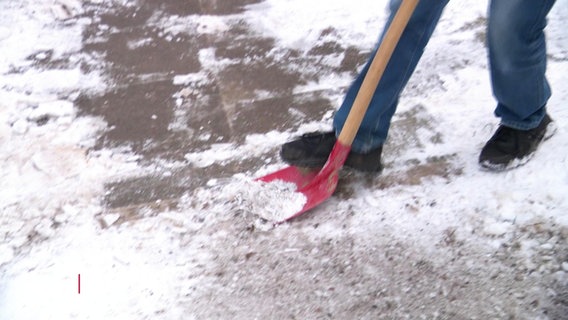 Ein Anwohner befreit einen Gehweg mit einer Schaufel von Schnee und Eis. © Screenshot 
