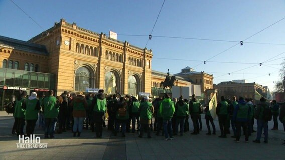 Eine Gruppe von Demonstranten steht vor einem Bahnhofsgebäude. © Screenshot 