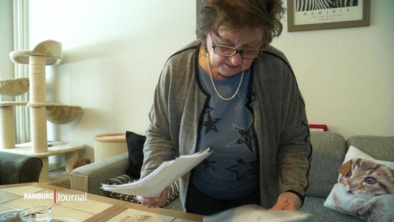 Eine Frau schaut auf Unterlagen, die auf einem Wohnzimmertisch liegen. © Screenshot 