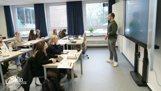 Ein Lehrer und Schülerinnenin in einem Klasseraum. © Screenshot 