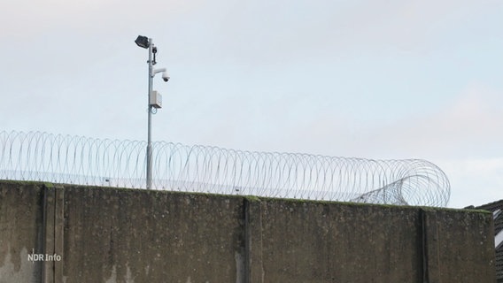 Eine Gefängnismauer mit Stacheldraht und einer Flutlichtanlage. © Screenshot 