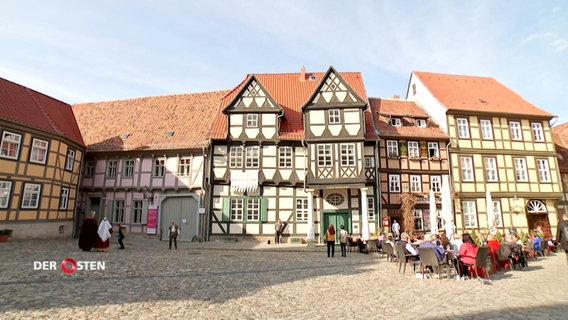 Ein Platz in Quedlinburg: Vor historischen, bunt bemalten Fachwerkhäusern sitzen Leute an Tischen eines Straßencafés. © Screenshot 