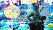 Ein Nachbau der Statue von Gotthold Ephraim Lessing vom Gänsemarkt unterwegs auf dem Hamburger Dom. Die Figur hält ein Schild mit der Aufschrift: "Lessing on Tour". © Screenshot 