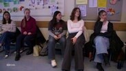 Mehrere Schüler*innen auf Schulstühlen nebeneinander sitzend. © Screenshot 