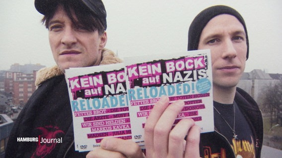 Zwei Männer halten einen Flyer in die Kamera "Kein Bock auf Nazis - reloaded". © Screenshot 