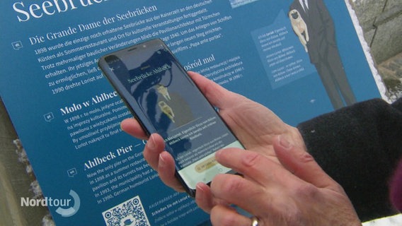 Eine Person hält ein Smartphone in der Hand und nutzt die App "Kaiserbäder Erlebnispfad". © Screenshot 