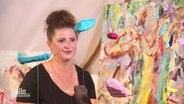 Künsterlin Zoë MacTaggart sitzt vor ihren Bildern. © Screenshot 