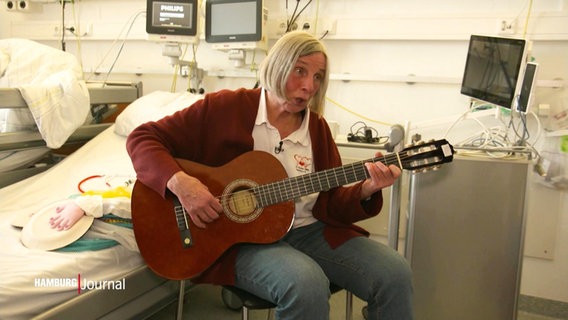Schwester Anne von der Kinderherzstation im UKE sitzt auf einem Krankenbett und spielt Gitarre. © Screenshot 