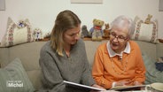 Svenja und Friedegund Möller sitzen auf dem Sofa und betrachten ein Buch. © Screenshot 