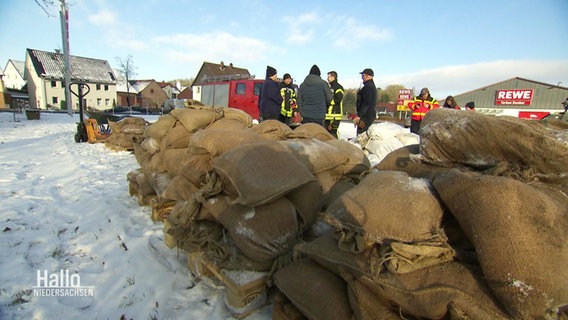 Eine Gruppe von Angehörigen einer Freiwilligen Feuerwehr stehen hinter einem Haufen Sandsäcke. © Screenshot 