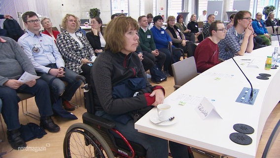 Menschen, die in Rollstühlen und Stühlen sitzen in einem Kongressraum. © Screenshot 