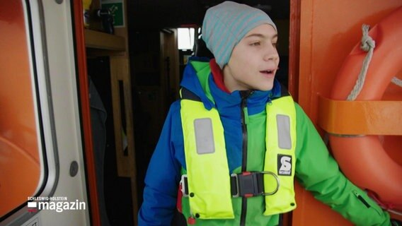 Ein Junge mit Mütze und Schwimmweste steht auf einem Schiff © Screenshot 