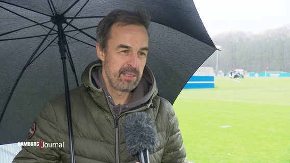 Reporter Lars Pegelow neben dem Fußballplatz unterm Regenschirm. © Screenshot 