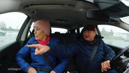 Ein Rentner-Paar sitzt in einem Auto, der Fahrer zeigt aus dem Fenster, seine Frau schaut hin. © Screenshot 