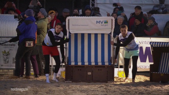 Zwei Männer tragen einen Strandkorb bei einem Wettbewerb. © Screenshot 