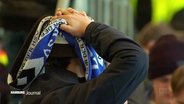 Ein HSV-Fan mit Fan-Schal im Stadion schlägt die Hände über dem Kopf zusammen. © Screenshot 