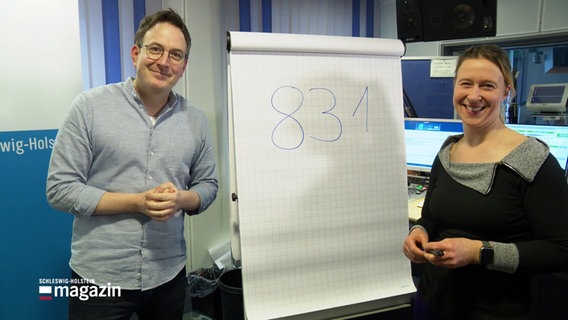 Eine Moderatorin und ein Moderator von NDR 1 Welle Nord stehen neben einem Flipchart, auf dem die Zahlen 831 aufgeschrieben stehen. © Screenshot 