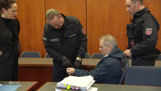 Der angeklagte Göttinger Anwalt Reiner Fuellmilch im Gerichtssaal; ein Justizbeamter löst seine Handschellen. © Screenshot 