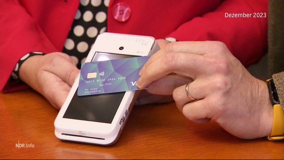 Eine Bezahlkarte wird ein Kartenlesegerät gehalten. © Screenshot 