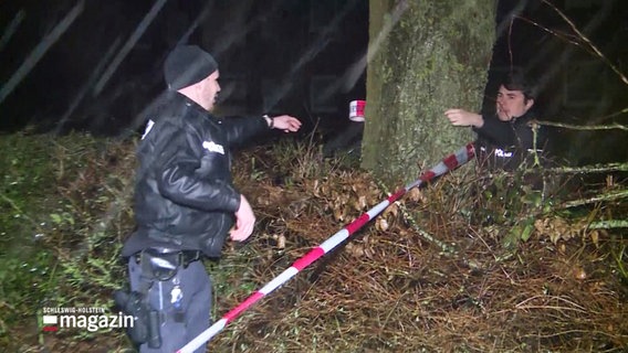 Polizisten befestigen Absperrband an einem Baum. © Screenshot 