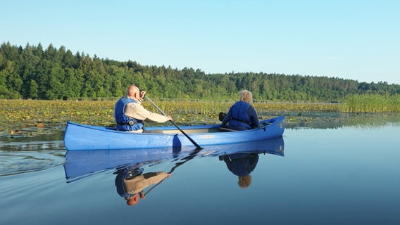 Eine Frau und ein Mann sitzen in einem blauen Kanu und rudern über sehr flaches Gewässer. © Screenshot 