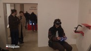Ein Besucher der Ausstellung sitzt mit einer VR-Brille auf einem Stuhl. © Screenshot 