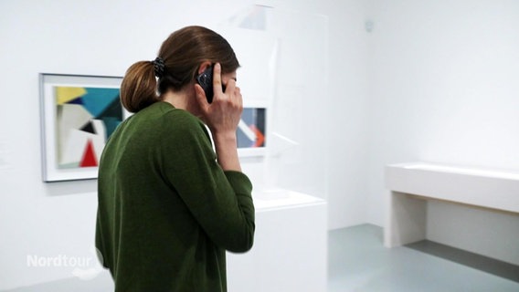 Eine Frau geht telefonierend durch eine Kunstausstellung. © Screenshot 