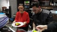 Zwei Menschen richten buntes Essen auf einem Teller an. © Screenshot 
