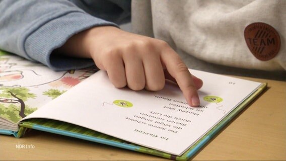 Nahaufnahme eines Kindes dessen hand beim Lesen in einem Buch liegt. © Screenshot 