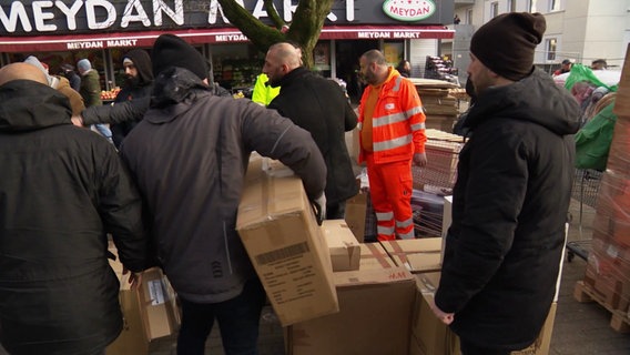 Mehrere Männer sortieren auf einem Platz Kartons und Kisten mit Hilfsmaterial für Erdbebenopfer in Syrien und der Türkei © NDR 