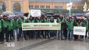 Mitglieder einer Gewerkschaft stehen vor einem Bahnhof. © Screenshot 