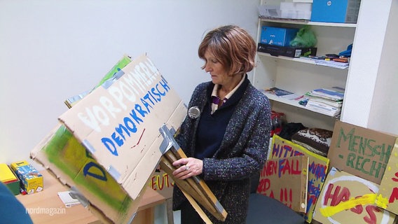 Eine Frau hält mehrere Schilder mit politischen Parolen in den Händen. © Screenshot 
