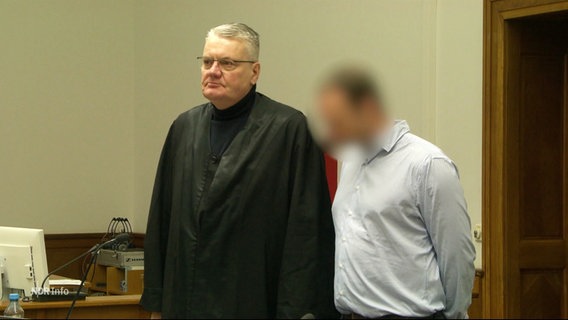 Ein Angeklagter steht neben seinem Anwalt in einem Gerichtssaal. © Screenshot 