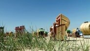 Menschen sitzen in Strandkörben am Meer und genießen die Sonne. © Screenshot 