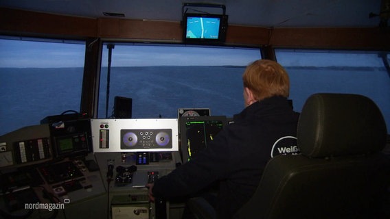 Auf der Brücke einer Fähre: Der Kapitän von hinten zu sehen sowie Navigationsintrumente und vor den Fenstern das Meer. © Screenshot 