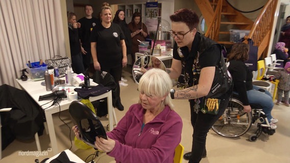 Anja Voigt, Organisatorin der Aktion "Barber Angels Brotherhood", hält nach dem Haareschneiden einen Spiegel neben den Hinterkopf ihrer Kundin, einer älteren Dame. © Screenshot 