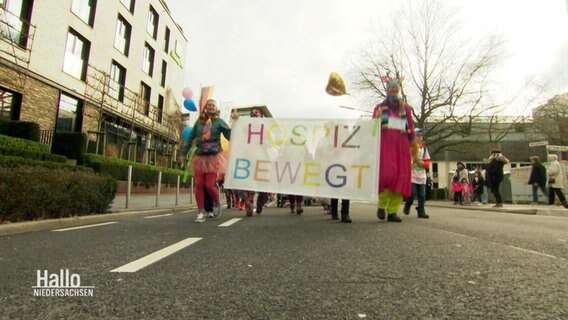 Karnevalisten halten ein Plakat mit der Aufschrift "Hospiz bewegt". © Screenshot 