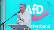 Holm auf einer Bühne mit AfD-Logo dahinter. © Screenshot 