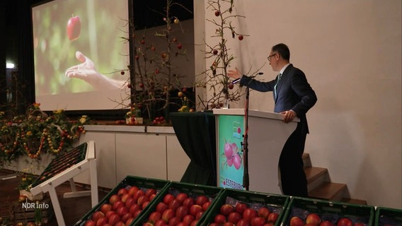 Cem Özdemir auf einer Bühne mit Obstkisten um ihn herum. © Screenshot 