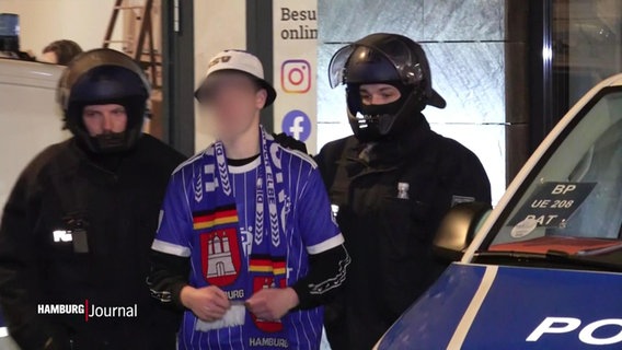 Ein HSV-Fan wird von zwei Polizisten begleitet. © Screenshot 