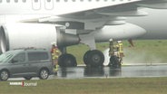 Feuerwehrleute untersuchen den geplatzten Reifen eines Flugzeugs auf einer Rollbahn. © Screenshot 