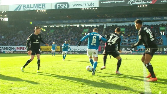 Ein Spieler von Hansa Rostock nimmt es auf dem Platz direkt mit drei Fußballern des HSV auf. © Screenshot 
