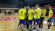 HC Empor Rostock steht nach einem Spiel zusammen im Kreis in der Handballhalle. Im Hintergrund jubelt MTV Braunschweig. © Screenshot 