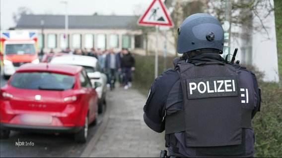 Ein Polizist steht an einer Straße vor einer Schule. © Screenshot 