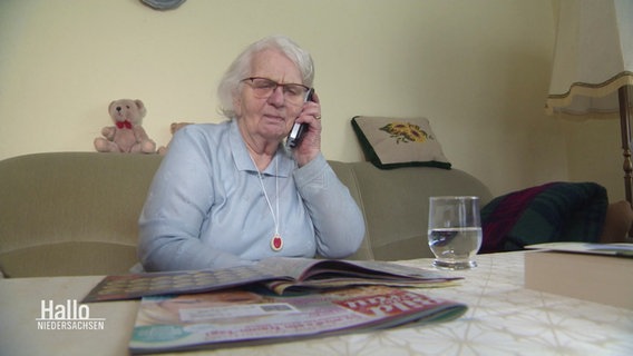 Eine ältere Dame sitzt auf einem Sofa und hat den Hörer eines Festnetztelefons am Ohr. © Screenshot 