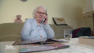 Eine ältere Dame sitzt auf einem Sofa und hat den Hörer eines Festnetztelefons am Ohr. © Screenshot 