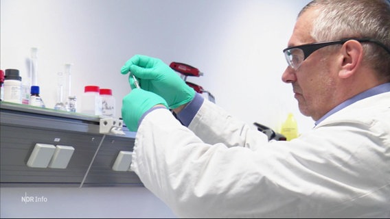 Ein Mann mit Schutzbrille und grünen Gummihandschuhen untersucht etwas im Labor © Screenshot 