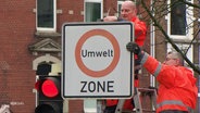 Arbeiter entfernen das Umwelt-Zonen-Verkehrsschild. © Screenshot 